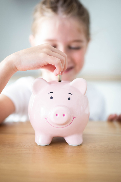 child putting money in piggy bank